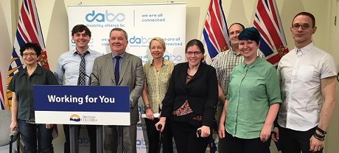 DABC staff standing with Minister Shane Simpson in front of the DABC banner and several BC flags